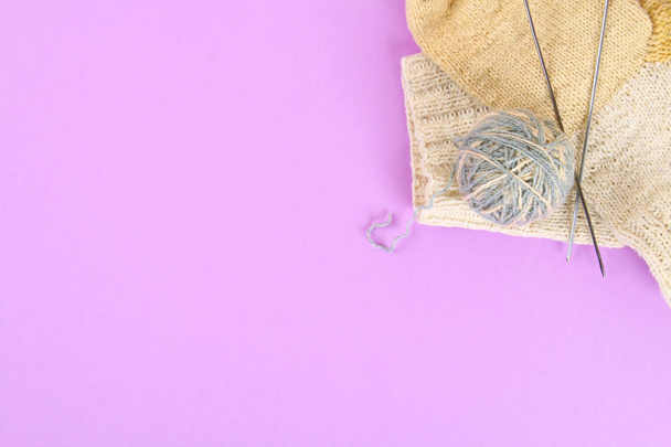 A ball of wool with knitting needles and knitted socks on a color pastel table. Needlework - 写真・画像