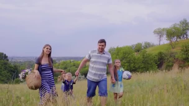Fiatal, boldog család, három gyermek megy a piknik zöld dombok. 4k - Felvétel, videó