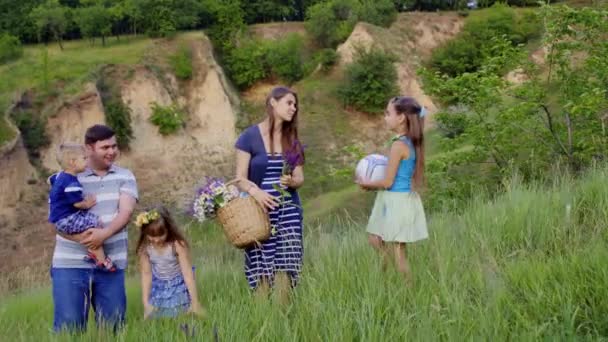 Νέοι ευτυχισμένη οικογένεια με τρία παιδιά πρόκειται για πικ-νικ σε καταπράσινους λόφους. 4k - Πλάνα, βίντεο
