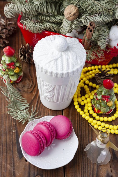 White cup and pink macaroons with christmas decorations on wooden background.Focus on cup - Photo, Image