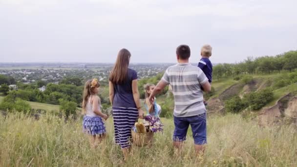 Jonge gelukkig gezin met drie kinderen gaan voor picknick in de groene heuvels. 4k - Video