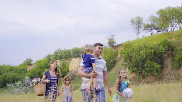 Молодая счастливая семья с тремя детьми отправляется на пикник в зеленые холмы. 4K
 - Кадры, видео