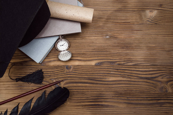 Capa graduada, relógio de bolso, pilha de livros, caneta de penas e diploma de rolagem na mesa da escola de madeira com espaço de cópia
. - Foto, Imagem