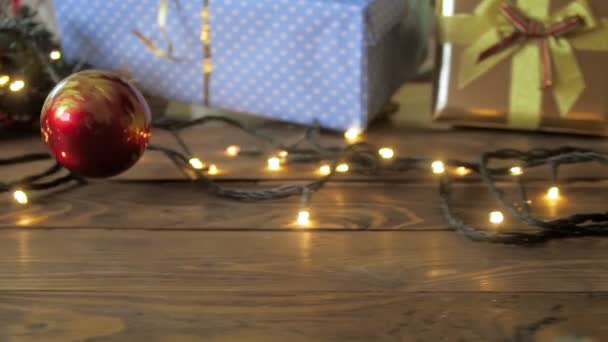 Slow-motion video van rode Kerstbal vallen en rollen op houten tafel - Video