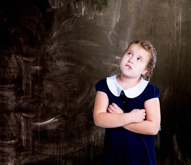 thoughtful  little girl   at school against chalkboard  - 写真・画像