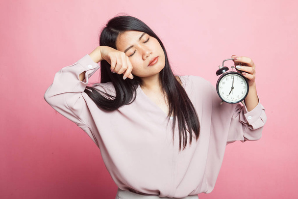 Sleepy young Asian woman with a clock in the morning on pink background - Zdjęcie, obraz