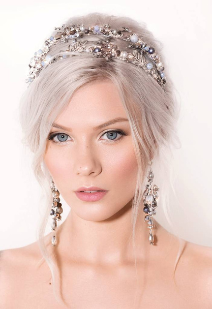 Beautiful young blond woman posing in crown and earrings in studio - Foto, Imagen