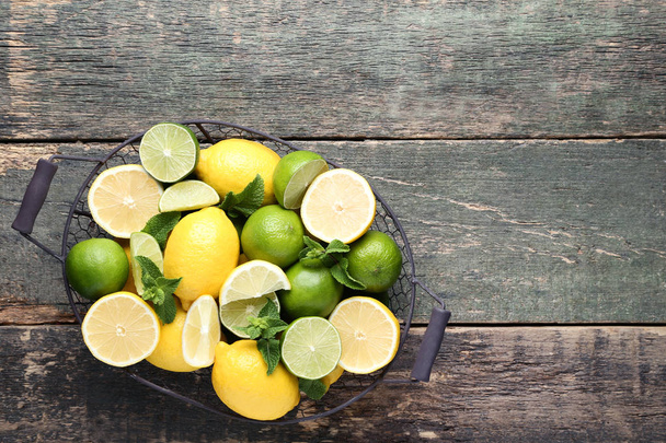fresh whole and halved Lemons and limes with mint leaves in basket on grey wooden table - Foto, imagen