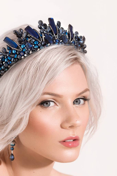 schöne junge blonde Frau posiert mit Krone und Ohrringen im Studio - Foto, Bild