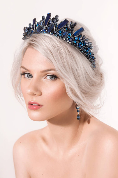 Beautiful young blond woman posing in crown and earrings in studio - Photo, image