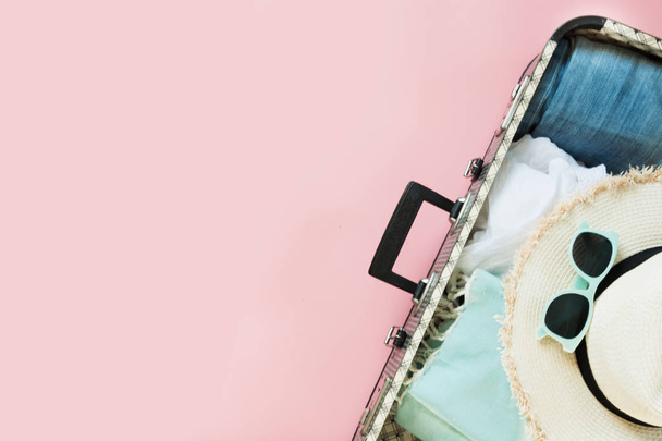Open suitcase with female clothes for trip on pastel pink background. Top view with copy space. Summer concept travel. - Photo, image