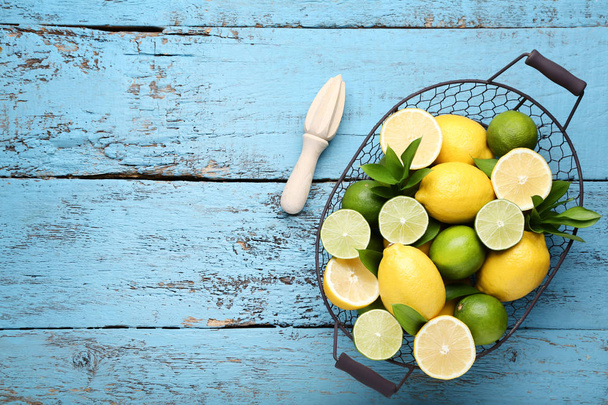 whole and halved Lemons and limes with green leaves in basket on blue wooden table - Φωτογραφία, εικόνα