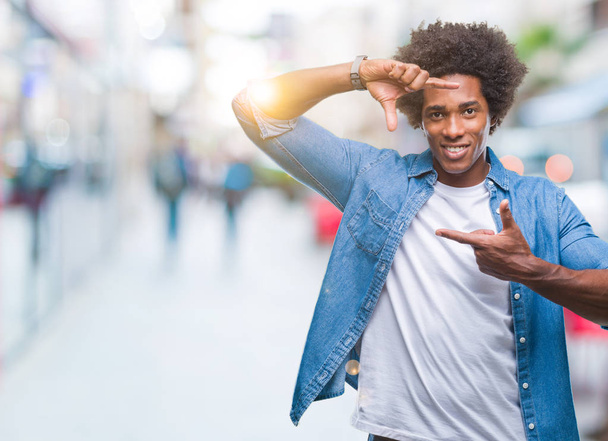 Hombre afroamericano sobre fondo aislado sonriendo haciendo marco con manos y dedos con cara feliz. Concepto de creatividad y fotografía
. - Foto, imagen