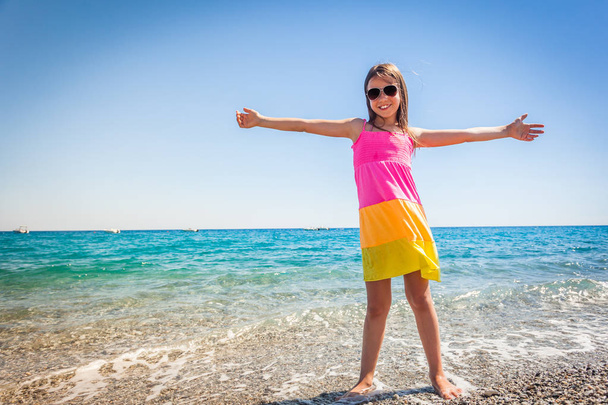 Enfant féminin en robe d'été colorée sur une plage profitant de la mer avec de l'eau turquoise, concept de vacances scolaires
 - Photo, image