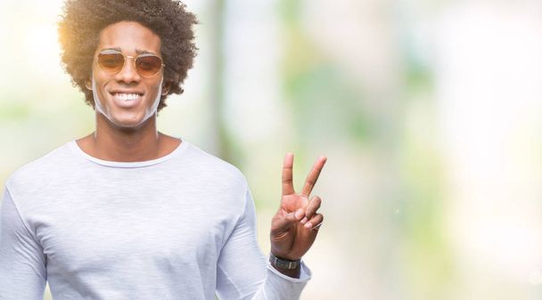 Afro amerikkalainen mies aurinkolasit yli eristetty tausta hymyillen onnellinen kasvot silmää kamera tekee voitonmerkki. Numero kaksi.
. - Valokuva, kuva