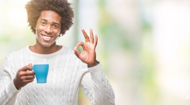 Афро-американец пьет чашку кофе на изолированном фоне делает ОК знак с пальцами, отличный символ
 - Фото, изображение