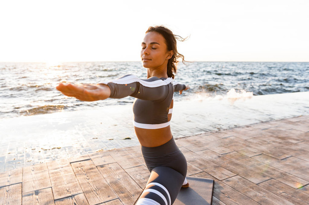 Picture of young fitness lady outdoors in the beach make yoga stretching exercises. - Photo, image
