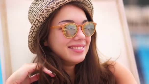 Pretty girl in hat and sunglasses smiling and adjusting her hair. Girl on rest - Πλάνα, βίντεο