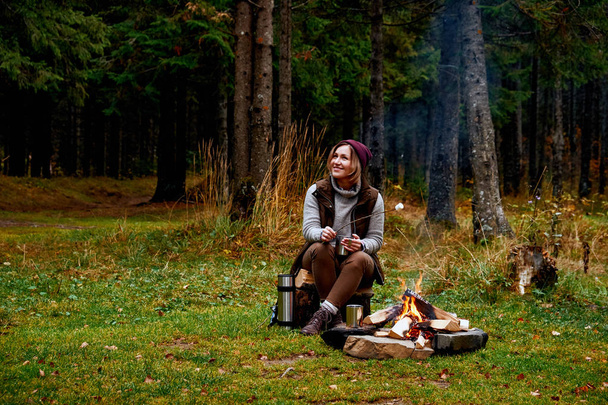 Wanderlust and Travel concept. Woman roast marshmallow candies on the campfire in forest. Spring or autumn camping - Foto, immagini
