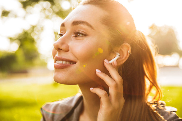 Picture of beautiful cute fitness sports woman in park outdoors listening music with earphones. - Foto, Imagem