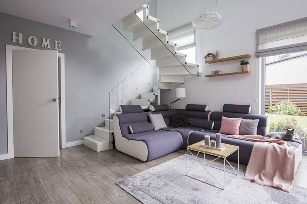 Corner sofa with pink blanket next to stairs in apartment interior with door and table. Real photo - Zdjęcie, obraz