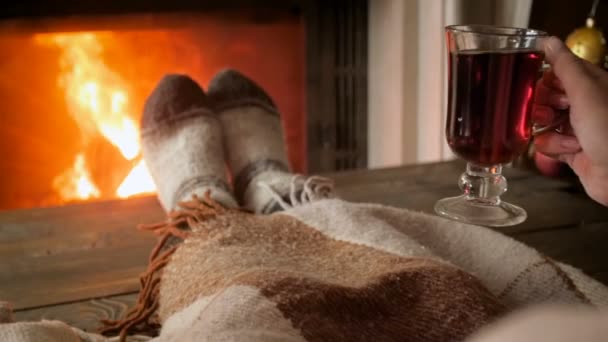 Closeup slow motion video of woman warming feet at fireplace and drinking hot tea - Footage, Video