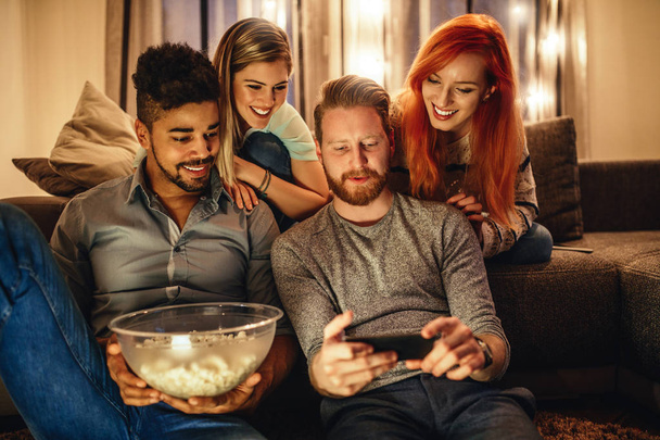 Two young man and two young women looking at a mobile phone - Photo, Image