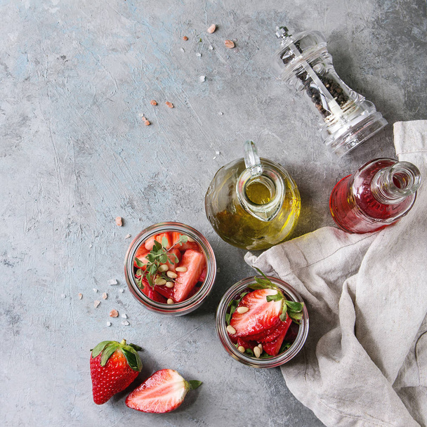 Beetroot and strawberry salad served with arugula and nuts in glass jars with cloth and bottles of fruit ocet and olive oil over grey texture background. Top view, space. Healthy eating. Square image - Zdjęcie, obraz