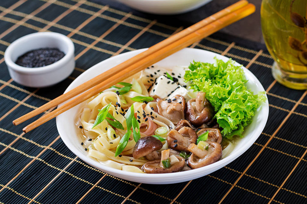 Vegan noodlesoep met tofu kaas, shiitake paddestoelen en sla in witte kom. Aziatisch eten. - Foto, afbeelding