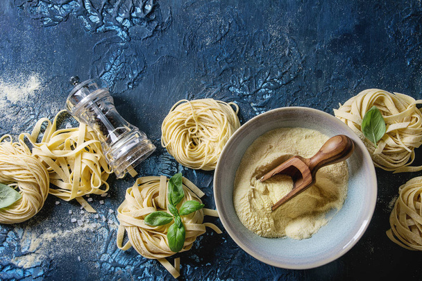 Variety of italian homemade raw uncooked pasta spaghetti and tagliatelle with basil leaves, olive oil, salt, pepper, semolina flour over dark blue texture background. Flat lay, copy space - Φωτογραφία, εικόνα