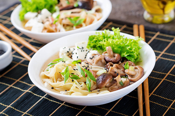 Vegan noodle soup with tofu cheese, shiitake mushrooms and lettuce in white bowl. Asian food. - Photo, Image