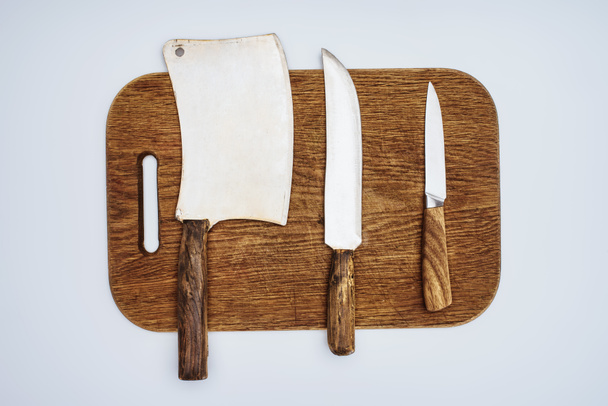 top view of different kitchen knives on wooden chopping board isolated on grey   - Photo, Image