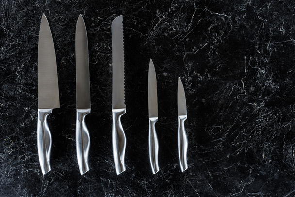 Ansicht von verschiedenen Küchenmessern auf schwarzer Marmoroberfläche mit Kopierraum  - Foto, Bild