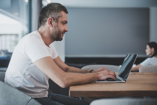 Zijaanzicht van lachende mannelijke freelancer laptop met leeg scherm thuis  - Foto, afbeelding