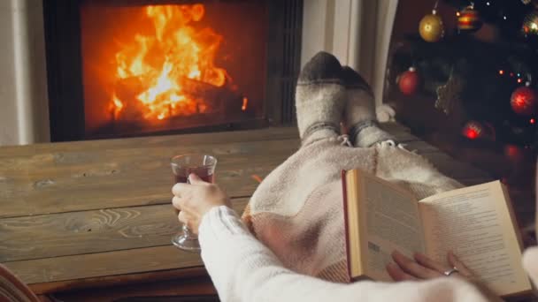 SLow motion footage of woman reading book and drinking tea next to burning fireplace on Christmas eve - Footage, Video
