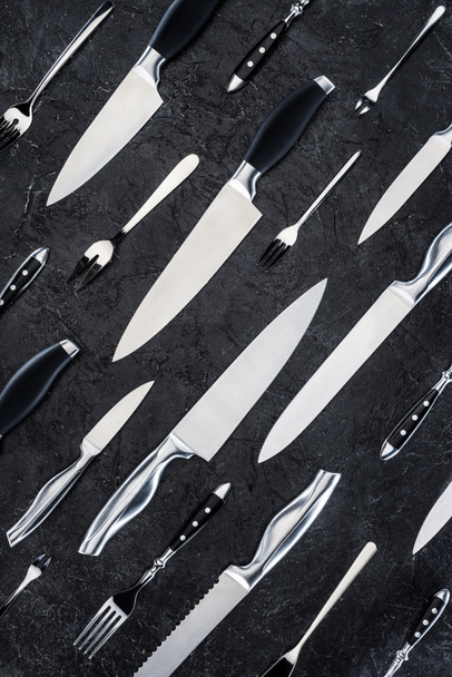 Κάτοψη των διαφόρων πιρούνια και μαχαίρια στη μαύρη επιφάνεια - Φωτογραφία, εικόνα