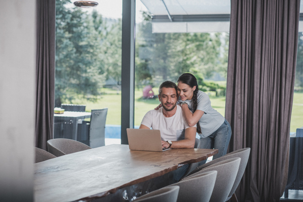 selective focus of woman embracing boyfriend while he using laptop at home - Valokuva, kuva