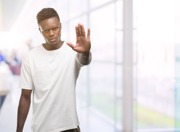 Beyaz t-shirt giyen genç Afro-Amerikan adam elin avuç ile şarkı stop yapıyor. Negatif ve ciddi bir jest yüz ifadesiyle uyarı. - Fotoğraf, Görsel