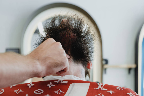ein junger gutaussehender bärtiger Mann in einem Friseurladen. der Friseur bürstet sich die Haare und schneidet sie mit einem elektrischen Trimmer. - Foto, Bild