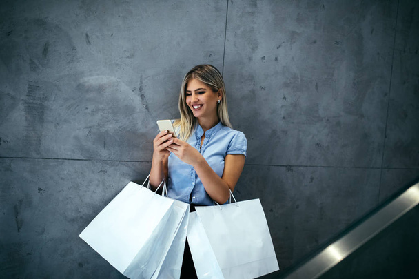 Young woman holding shopping bags and using her phone - Photo, image