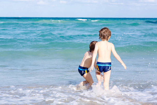 Dos niños felices corriendo en la playa del océano. Divertidos niños lindos, hermanos, gemelos y mejores amigos haciendo vacaciones y disfrutando del verano en el día de verano soleado tormentoso. Miami, Florida
 - Foto, imagen