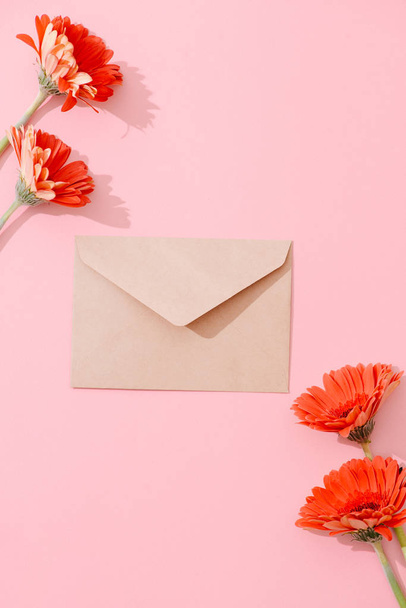 Blank greeting card with brown envelope and gerbera flowers on pink table with vintage and vignette tone - Fotó, kép