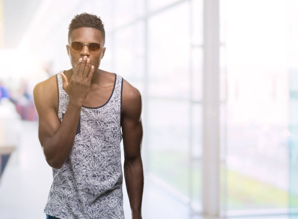 junger afrikanisch-amerikanischer Mann mit Sonnenbrille bedeckt Mund mit Hand geschockt vor Scham für Fehler, Ausdruck von Angst, Angst in der Stille, geheimes Konzept - Foto, Bild