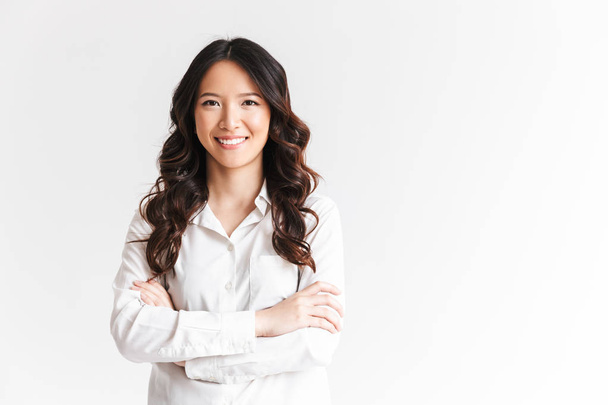 Portrait of gorgeous asian woman with long dark hair looking at camera with beautiful smile and arms crossed isolated over white background in studio - Foto, afbeelding