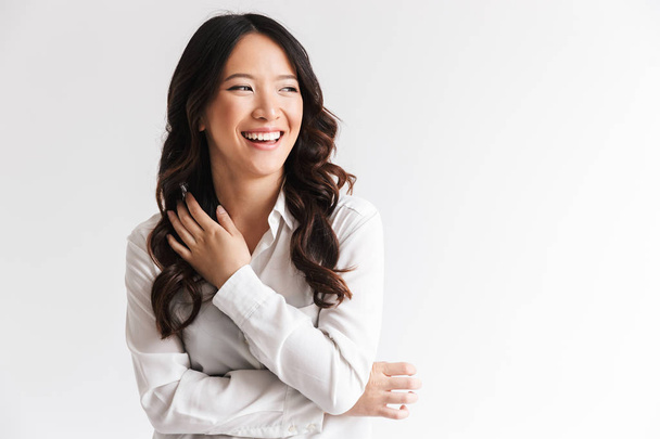 Image of charming chinese woman with long dark hair looking aside at copyspace and laughing isolated over white background in studio - Фото, зображення
