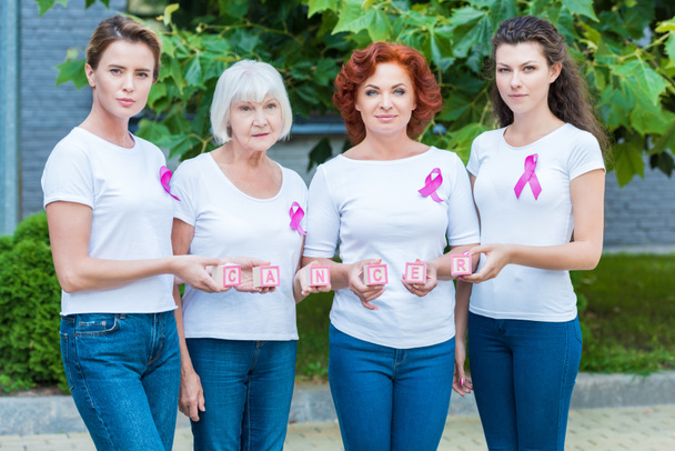 mujeres con cintas de conciencia de cáncer de mama sosteniendo cubos con cáncer de palabra y mirando a la cámara
 - Foto, imagen