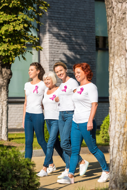 smiling women with breast cancer awareness ribbons holding hands and walking together  - Photo, Image