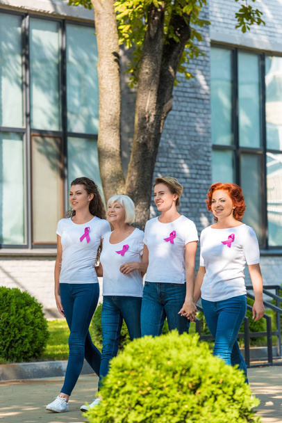 happy women with breast cancer awareness ribbons holding hands and walking together  - Photo, Image
