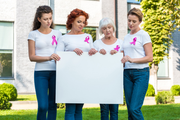 women with breast cancer awareness ribbons holding blank banner and looking down - Фото, зображення