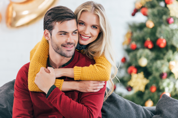 smiling girl hugging her boyfriend at home with christmas tree - Foto, imagen